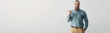 panoramic shot of handsome businessman in shirt showing thumb up and looking at camera 