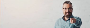 panoramic shot of handsome businessman in shirt pointing with finger and looking at camera 