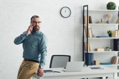handsome businessman in shirt talking on smartphone and looking away 