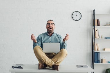handsome businessman in shirt and glasses sitting on table and holding laptop 