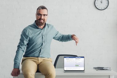 KYIV, UKRAINE - AUGUST 27, 2019: handsome businessman in shirt pointing with finger at laptop with facebook website 