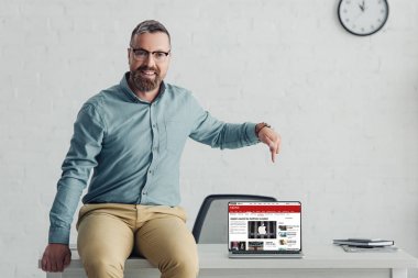 KYIV, UKRAINE - AUGUST 27, 2019: handsome businessman in shirt pointing with finger at laptop with bbs website