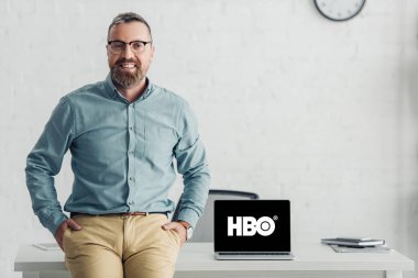 KYIV, UKRAINE - AUGUST 27, 2019: handsome businessman sitting on table near laptop with hbo logo