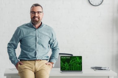 handsome businessman sitting on table near laptop with online trade website 