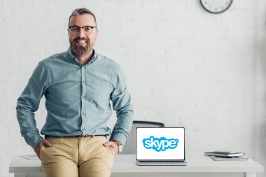 Kiev, Ukrayna - 27 Ağustos 2019: Skype logolu dizüstü bilgisayarın yanında masada oturan yakışıklı işadamı