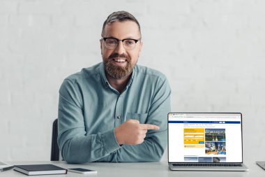 Kiev, Ukrayna - 27 Ağustos 2019: rezervasyon web sitesi ile dizüstü bilgisayar parmak ile işaret gömlek yakışıklı işadamı 