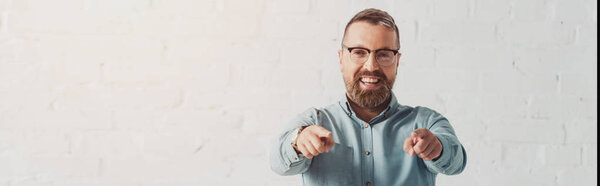 panoramic shot of handsome and smiling businessman in shirt pointing with finger 
