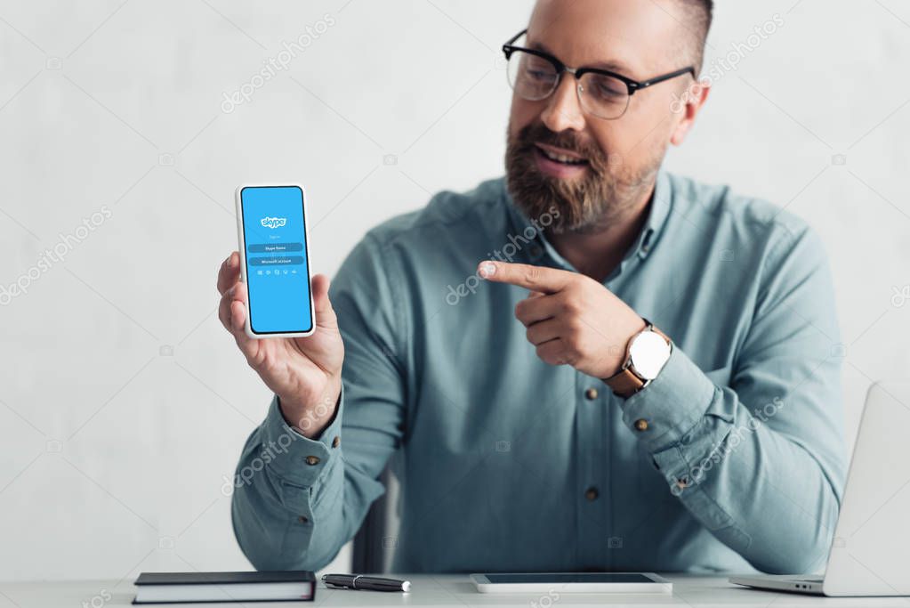 KYIV, UKRAINE - AUGUST 27, 2019: handsome businessman in shirt pointing with finger at smartphone with skype logo