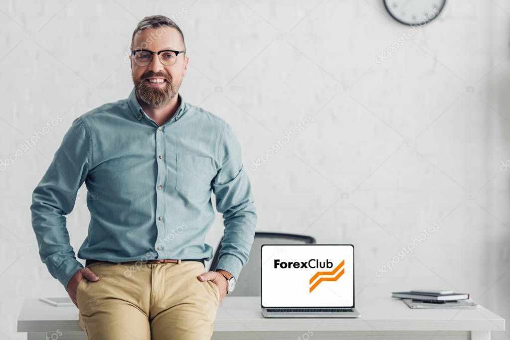 KYIV, UKRAINE - AUGUST 27, 2019: handsome businessman sitting on table near laptop with forex club logo