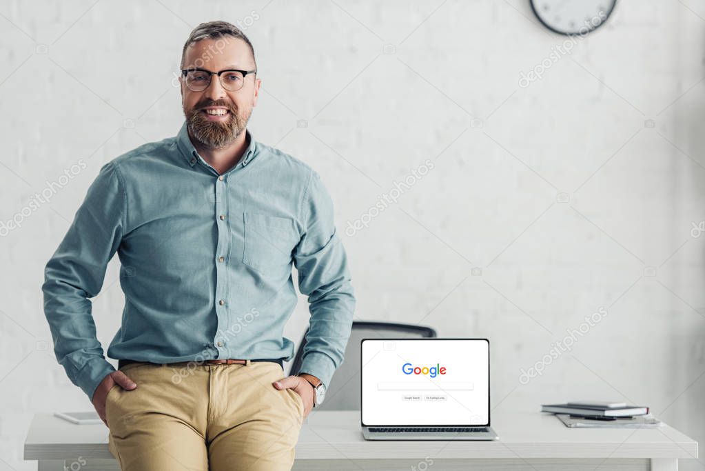KYIV, UKRAINE - AUGUST 27, 2019: handsome businessman sitting on table near laptop with google logo