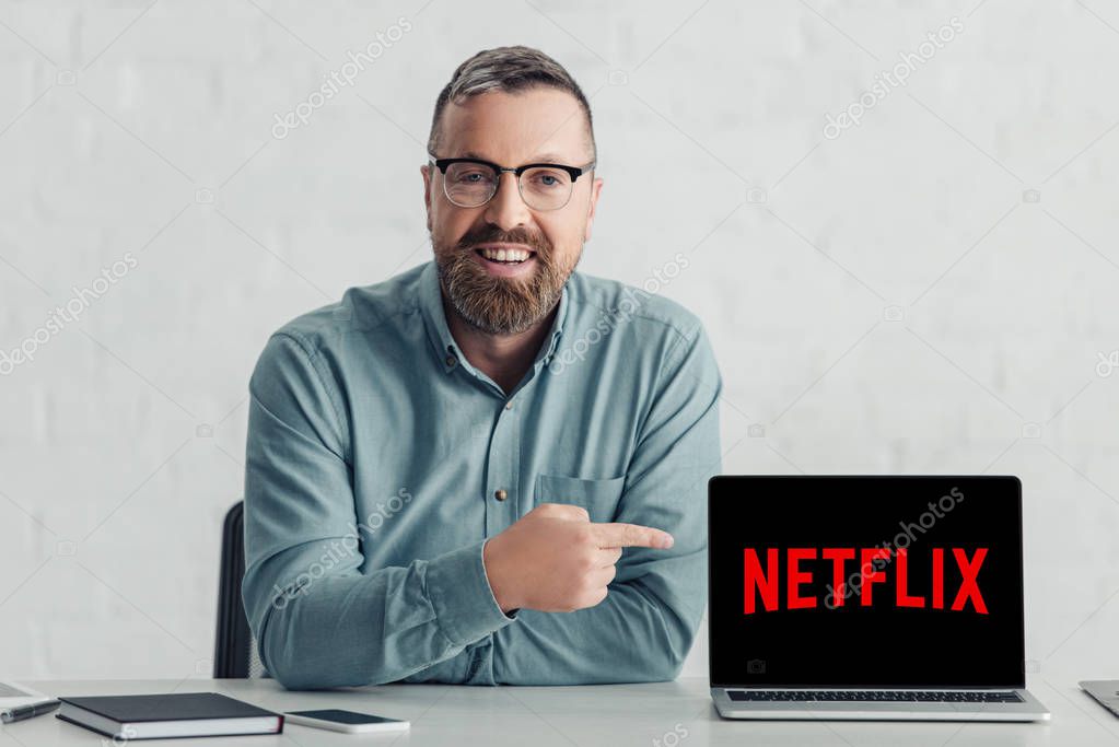 KYIV, UKRAINE - AUGUST 27, 2019: handsome businessman in shirt pointing with finger at laptop with netflix logo