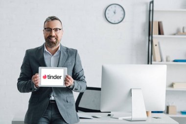 Kiev, Ukrayna - 27 Ağustos 2019: tinder logolu dijital tablet tutan resmi giyim yakışıklı işadamı