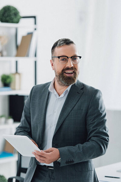 handsome businessman in formal wear and glasses using digital tablet in office 