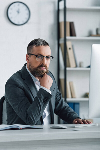 handsome businessman in formal wear and glasses looking at camera in office 