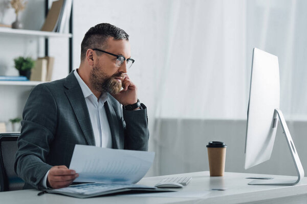 handsome businessman in formal wear talking on smartphone and holding document 