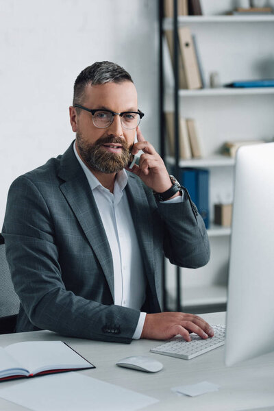 handsome businessman in formal wear talking on smartphone and looking at camera 