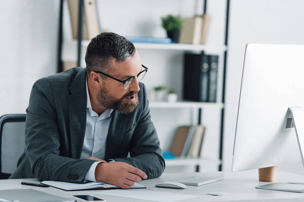 красивый бизнесмен в формальной одежде разговаривает на смартфоне и смотрит в компьютер
 