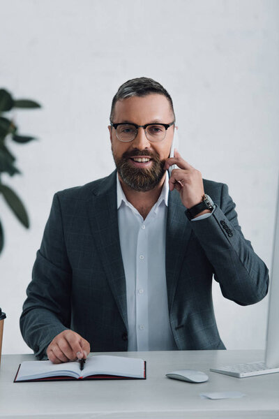 handsome businessman in formal wear talking on smartphone and looking at camera 
