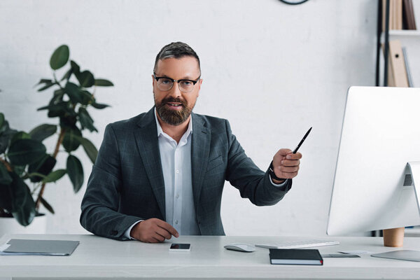 handsome businessman in formal wear holding pen and looking at camera 
