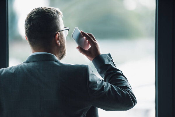 back view of man in formal wear holding smartphone 