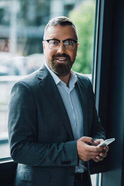 handsome businessman in formal wear and glasses holding smartphone 