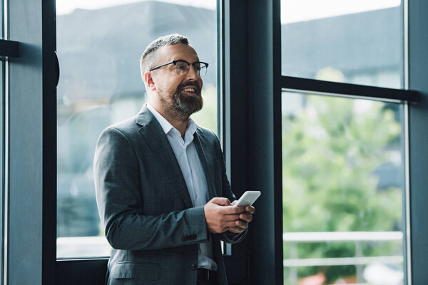 handsome businessman in formal wear and glasses holding smartphone 