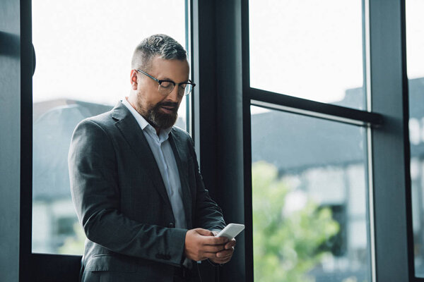 handsome businessman in formal wear and glasses holding smartphone 