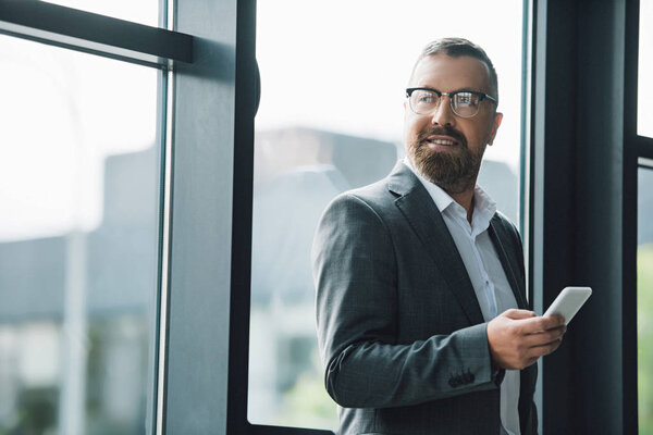 handsome businessman in formal wear and glasses holding smartphone 