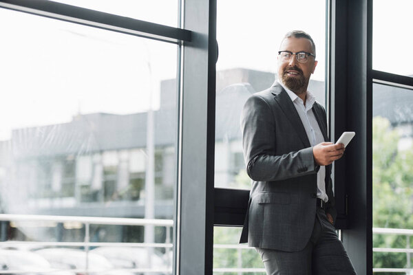 handsome businessman in formal wear and glasses holding smartphone 