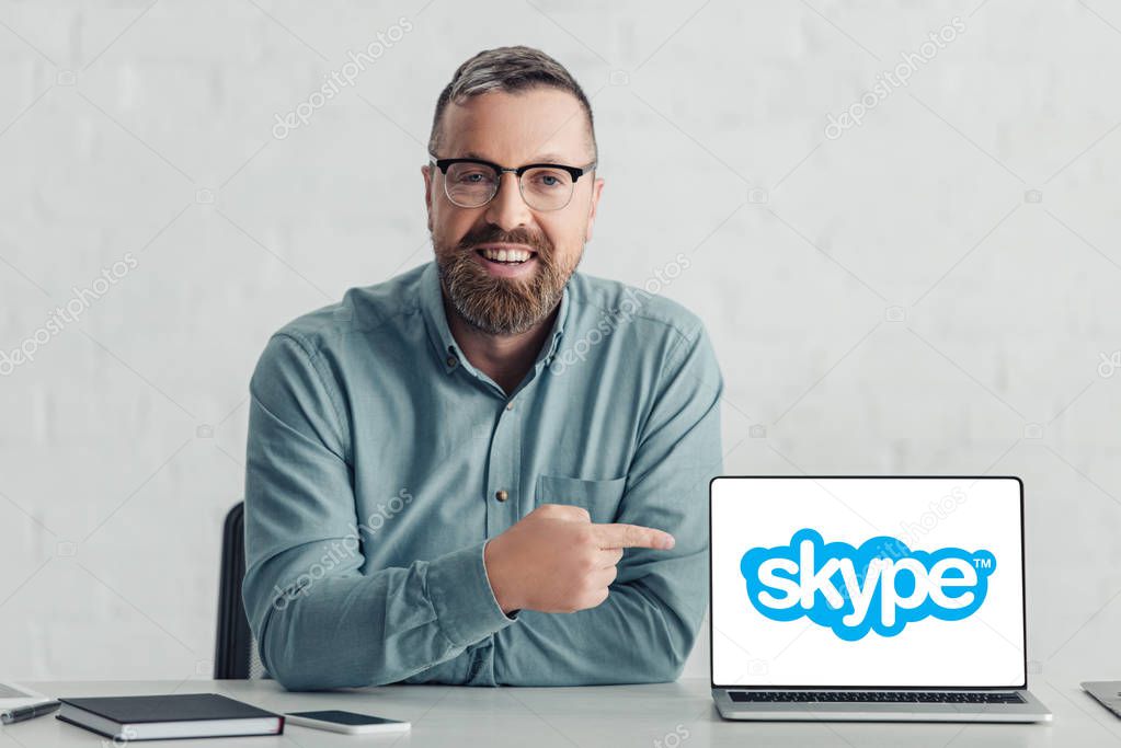 KYIV, UKRAINE - AUGUST 27, 2019: handsome businessman in shirt pointing with finger at laptop with skype logo
