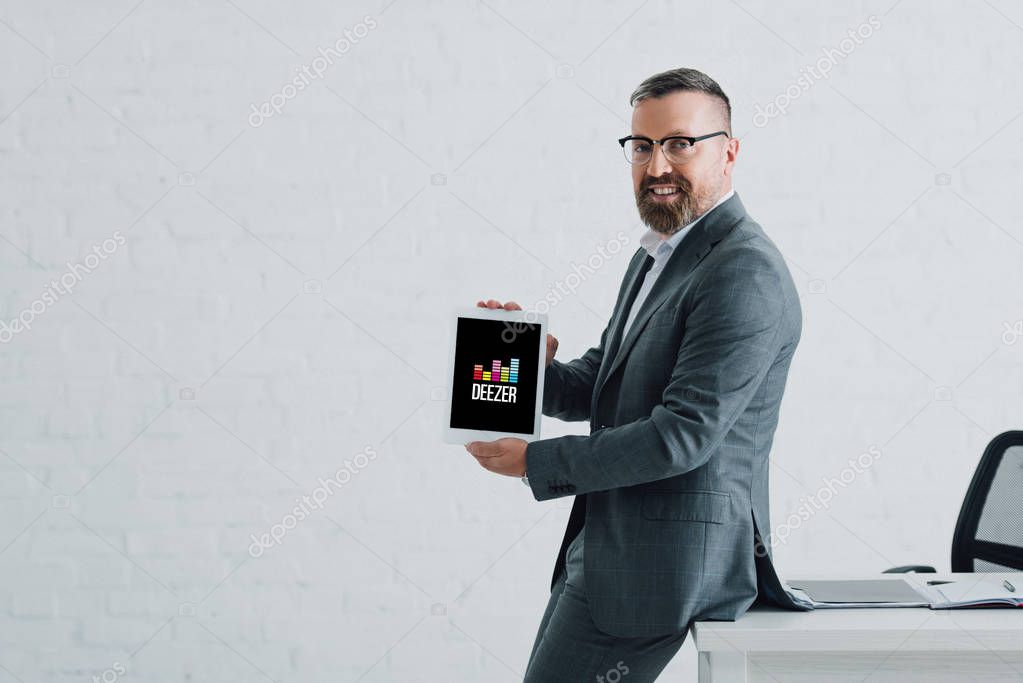KYIV, UKRAINE - AUGUST 27, 2019: handsome businessman in formal wear holding digital tablet with deezer logo