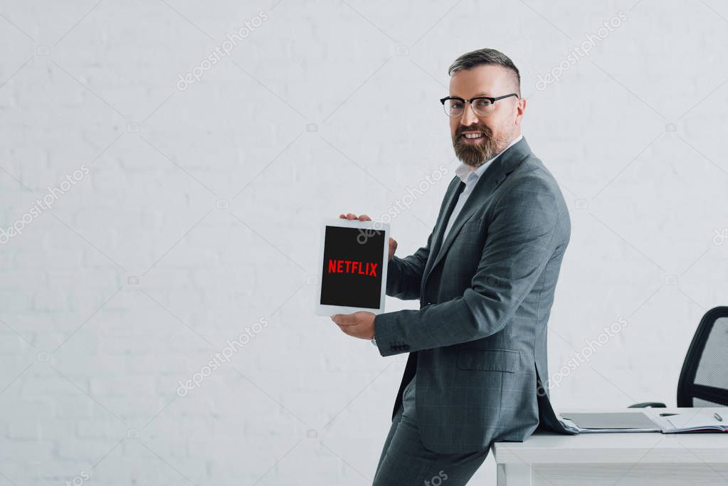 KYIV, UKRAINE - AUGUST 27, 2019: handsome businessman in formal wear holding digital tablet with netflix logo