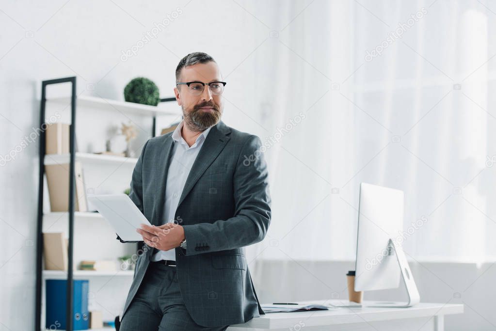 handsome businessman in formal wear and glasses using digital tablet in office 
