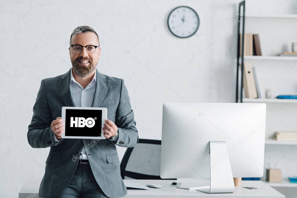 KYIV, UKRAINE - AUGUST 27, 2019: handsome businessman in formal wear holding digital tablet with hbo logo