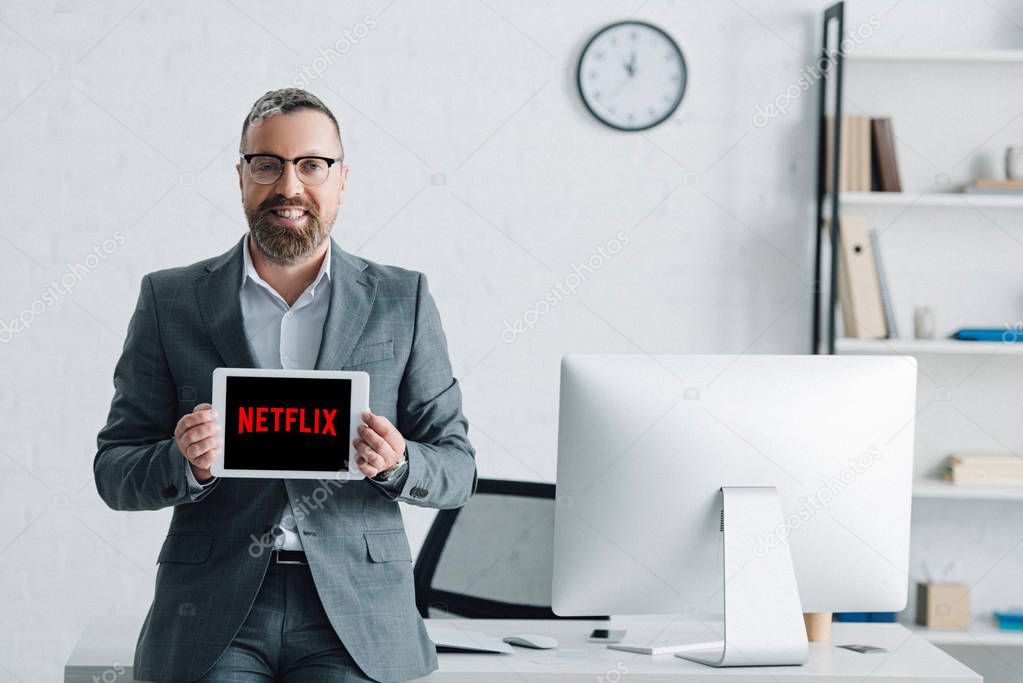 KYIV, UKRAINE - AUGUST 27, 2019: handsome businessman in formal wear holding digital tablet with netflix logo