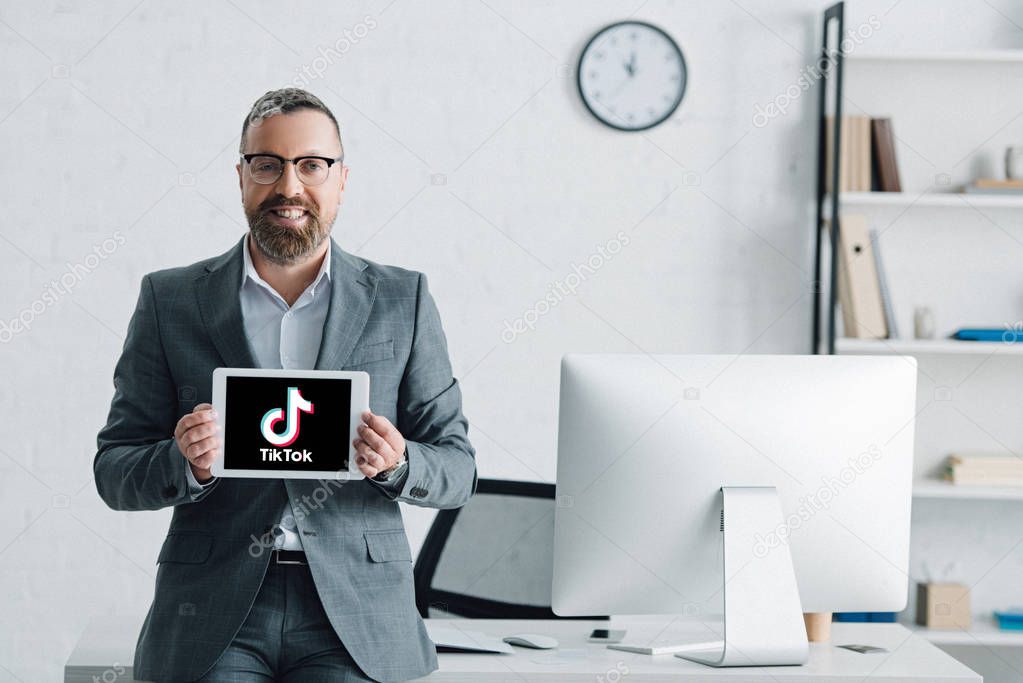 KYIV, UKRAINE - AUGUST 27, 2019: handsome businessman in formal wear holding digital tablet with tik tok logo