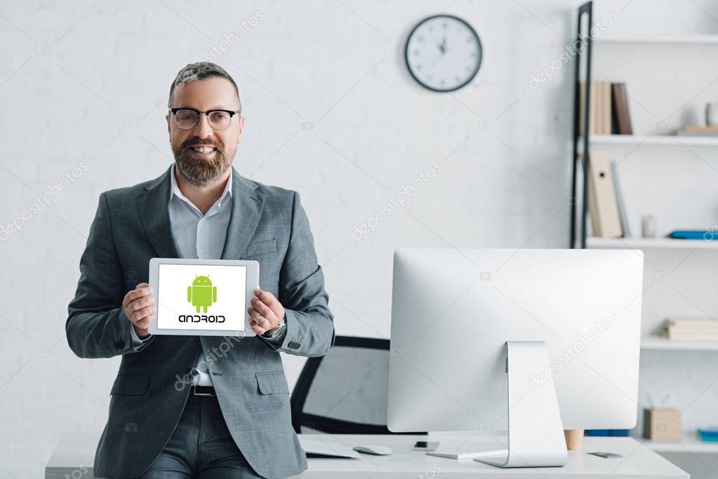 KYIV, UKRAINE - AUGUST 27, 2019: handsome businessman in formal wear holding digital tablet with android logo
