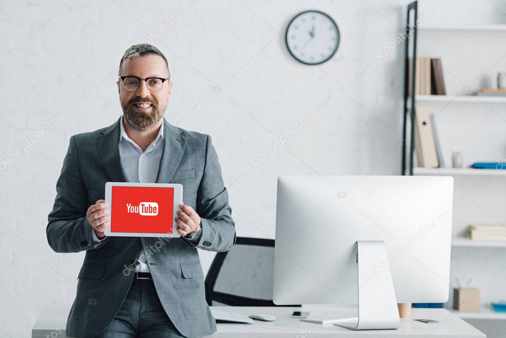 KYIV, UKRAINE - AUGUST 27, 2019: handsome businessman in formal wear holding digital tablet with youtube logo