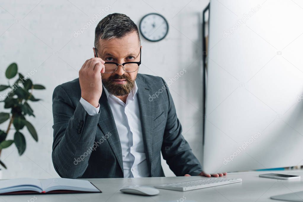 handsome businessman in formal wear and glasses looking at camera in office 