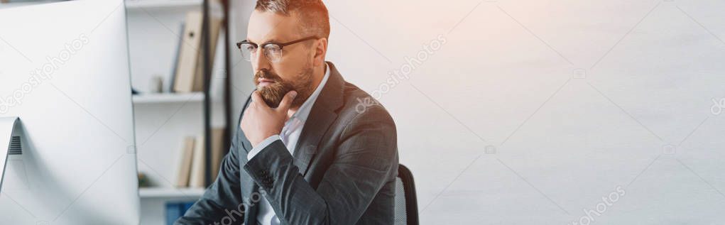 panoramic shot of handsome businessman in formal wear and glasses looking at computer 