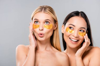 beautiful smiling asian and surprised european naked girls with eye patches isolated on grey clipart
