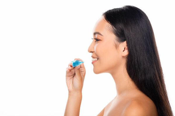 side view of smiling naked asian woman holding mouth guard isolated on white