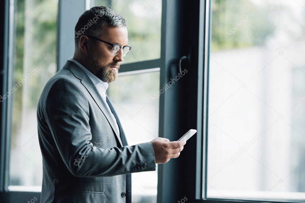 handsome businessman in formal wear and glasses holding smartphone 