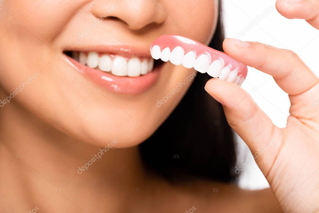 cropped view of woman holding false teeth isolated on white