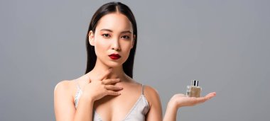 elegant asian woman in elegant dress with red lips holding perfume isolated on grey, panoramic shot clipart