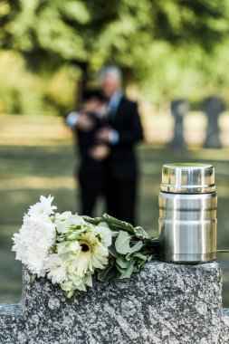 selective focus of flowers and mortuary urn on tombstone clipart