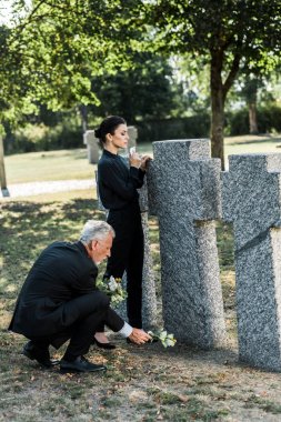 mezarlıkta mezarlar ve kadın yakın çiçek koyarak kıdemli adam 