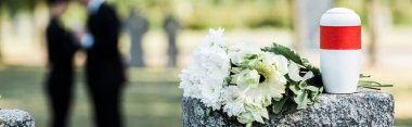 panoramic shot of white flowers and cemetery urn on tombstone clipart