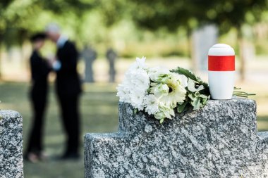 selective focus of bouquet of white flowers and cemetery urn on tombstone clipart
