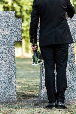 çiçekler tutan ve mezarların yanında duran üst düzey adam kırpılmış görünümü 